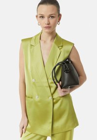 Jasnozielona satynowa kamizelka dwurzędowa z wyciętymi klapami i frontowymi kieszeniami, w zestawie z czarną teksturowaną mini torbą typu wiaderko.