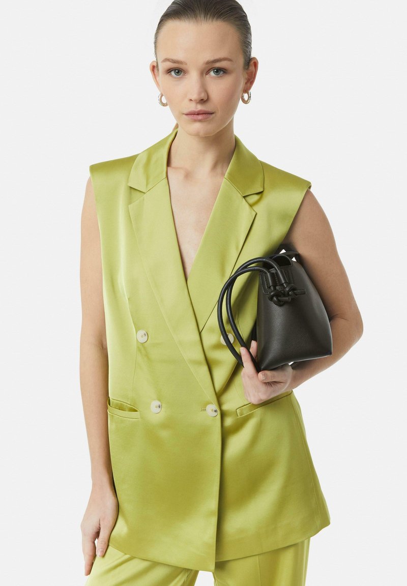Jasnozielona satynowa kamizelka dwurzędowa z wyciętymi klapami i frontowymi kieszeniami, w zestawie z czarną teksturowaną mini torbą typu wiaderko.