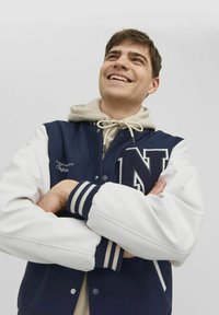 Marineblauwe en witte varsity-jas met een getextureerd wollen lijf, leren mouwen en een opvallende 'N'-patch. Voorzien van ribgebreide boorden en een beige capuchon eronder.