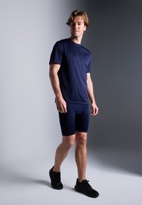 Camisola atlética azul marinho e calções justos combinados, feitos de tecido elástico, emparelhados com sapatilhas atléticas pretas.