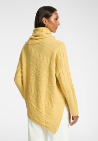 Maglione giallo lavorato a maglia con colletto alto, caratterizzato da un motivo a treccia e orlo a costine, progettato con una forma asimmetrica per un fit rilassato.