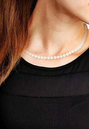 Collier de perles blanches avec des perles de taille uniforme, texture lisse et style classique, reposant sur un haut noir.