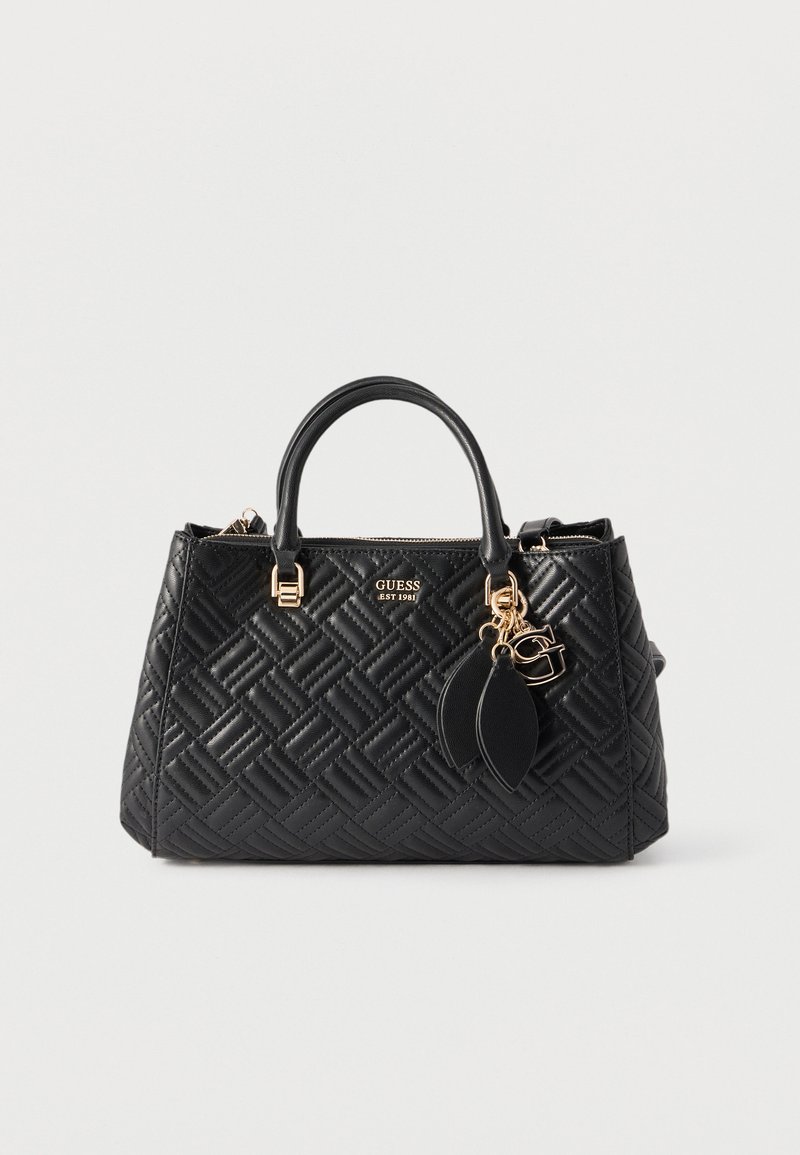 Μαύρη καπιτονέ δερμάτινη τσάντα με διπλές λαβές, χρυσά διακοσμητικά, διακοσμητικό γούρι και λογότυπο "GUESS EST 1981" στο μπροστινό μέρος.