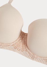 Beige gewatteerde beha met gladde cups en een band met kanten patroon, getoond op een witte achtergrond.