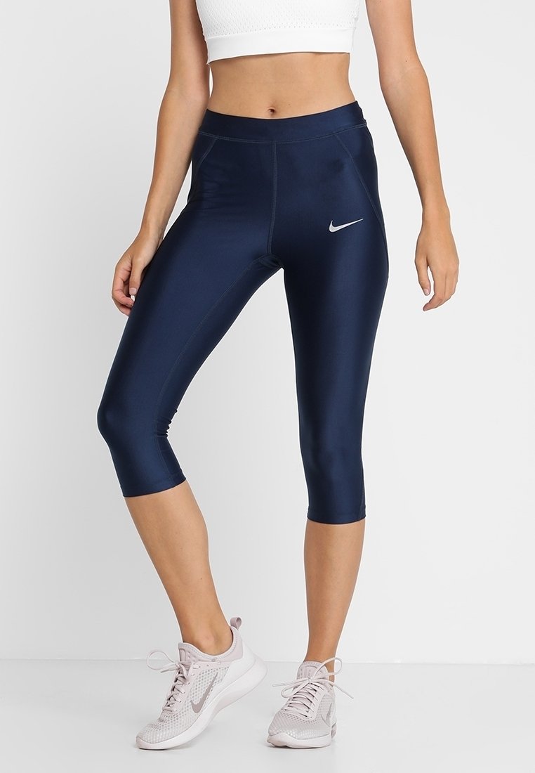 Leggings capri blu navy con una texture liscia e elastica. Presentano un logo Nike argentato sulla coscia sinistra e un design aderente.