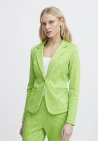 Zelený blazer s leopardím potiskem, přil�éhavý střih, klopové límce a dvě přední kapsy, kombinovaný s bílým topem. Hladká textilie.