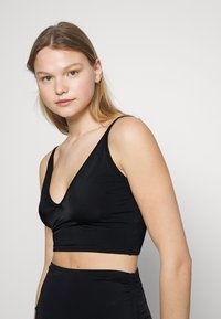 Top cropped preto com alças finas, decote em V profundo e tecido liso e elástico. Apresenta um design ajustado que realça a silhueta do corpo.