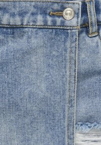 Gaiši zilas džinsa audums ar teksturētu apdari. Iekļautas metāla pogas, kontrastējošas šuves un nolietota zona gar apakšmalu.