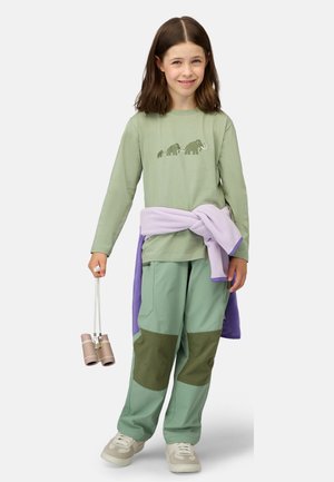 Long-sleeve light green shirt with elephant graphic, mint green pants with dark green patches, and a lavender fleece tied around the waist. Holding binoculars.