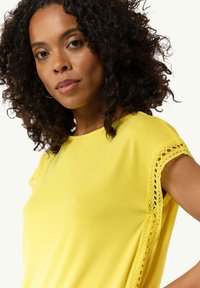 Bright yellow short-sleeve top with lace detailing on sleeves, smooth texture, relaxed fit, round neckline, and minimalistic design.