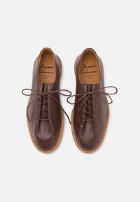 Brown leather lace-up shoes with a pebbled texture, rounded toe, and contrast stitching. Tan insoles feature brand logo and name.