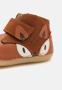 Zapato de cuero marrón para niños pequeños con diseño de zorro, que cuenta con una correa de gancho y bucle, acentos cosidos y una suela de goma color beige.