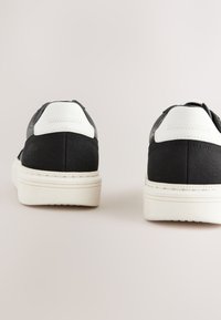 Baskets noires avec des accents blancs, présentant une tige texturée et un talon lisse. Semelles en caoutchouc avec des détails en relief pour l'adhérence.