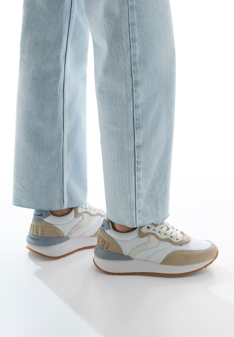 Sneakers in white and beige with light grey accents, featuring a textured finish, contrasting materials, and a rubber outsole.