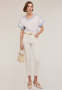 Blusa de algodón blanca con detalles a rayas en azul claro, combinada con pantalones blancos ajustados, bolso beige y zapatos pálidos con punta afilada.