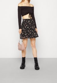 Černý crop top bez ramínek s řasením, ve spojení s černou květinovou skater sukni. Černé šněrovací boty a růžová kabelka dotvářejí outfit.