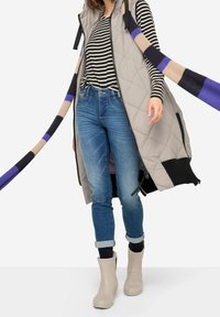 Tkaninowy szary kamizelka z bocznymi zamkami, czarnymi akcentami; w paski koszula z długim rękawem; niebieskie dżinsy; beżowe botki za kostkę; wielokolorowy dziany szalik.