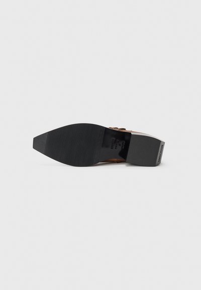 Suela de zapato de tacón marrón con una parte inferior de goma negra texturizada, que presenta un ligero diseño de cuña y un detalle de logo en relieve en el lateral.