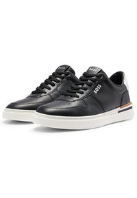 Sneaker in pelle nera con suola in gomma bianca, punta rotonda e chiusura con lacci. Presenta un logo sulla linguetta e un dettaglio a contrasto sul tallone.