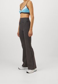 Sportbehå i blått och svart med tunna axelremmar; hög midja grå texturerade byxor med utsvängd ben; vita atletiska skor.