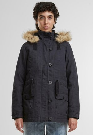 Parka noire avec capuche en fourrure, fermeture à boutons, deux poches frontales et cordons de serrage ajustables. Tissu texturé.