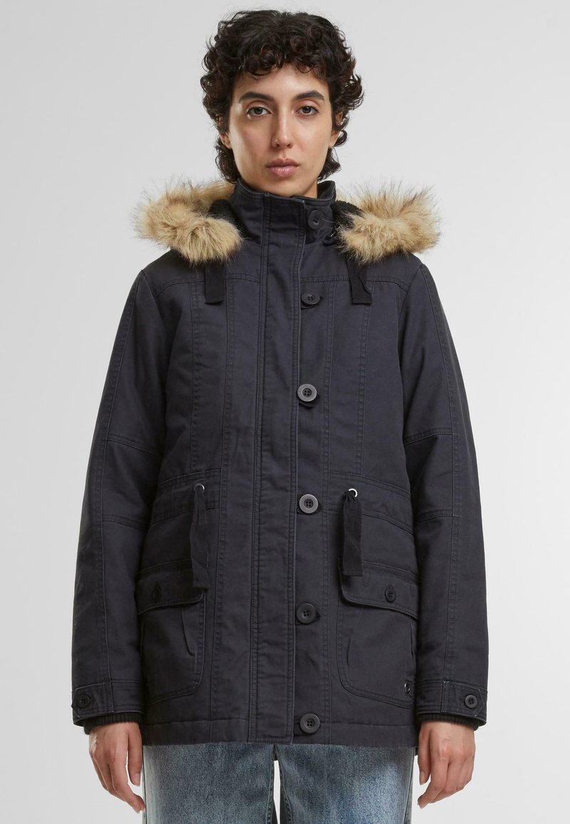 Črna parka jakna z kapuco obloženo z krznom, gumbnim zapiranjem, dvema sprednjima žepoma in nastavljivimi vrvicami. Ima teksturirano tkanino.