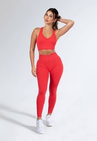 Reggiseno sportivo rosso e leggings a vita alta realizzati in tessuto elastico e liscio. Scarpe da ginnastica bianche completano il look sportivo.