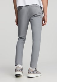 Szare spodnie slim fit wykonane z miękkiej mieszanki bawełny, z tylnymi kieszeniami i gładką teksturą, w połączeniu z szaro-białymi trampkami.