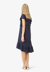 Tamsiai mėlyna suknelė su raukšlėtais trumpais rankovėmis ir platėjančiu apvadu. Pagaminta iš lygaus audinio, pasižymi laisvu siluetu ir kelio ilgio dizainu.