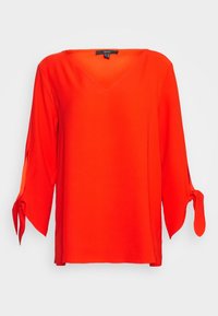 Rode V-halsblouse met driekwartmouwen, voorzien van verstelbare strikjes bij de manchetten en gemaakt van een soepele, lichte stof.