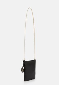 Borsa a tracolla rettangolare nera con tracolla in catena dorata e ciondolo rotondo nero con logo in rilievo dorato, su sfondo bianco.