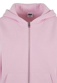 Sudadera con capucha rosa de tela suave, con capucha ajustable con cordón, bolsillos delanteros y cierre con cremallera plateada. Etiqueta visible en el interior del cuello.