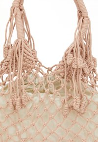 Macramé tote bag med et lyserødt knyttet design, der har frynser og en snøre-lukning, lavet af blødt, struktureret bomuldsstof.