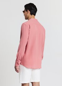 Long-sleeved shirt in soft coral fabric with a textured finish, featuring a classic collar and button cuffs, worn with white textured shorts.