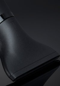 Tête de rasoir électrique noire avec un design incurvé et un bouton d'alimentation près du haut, sur un fond sombre et réfléchissant.