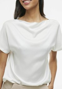 Hvit bluse med korte ermer laget av glatt stoff, med drapert halslinning og avslappet passform, som har myke folder og subtil glans.
