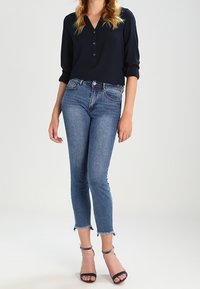 Marinblus med notchkrafter och trekvartsärmar, kombinerad med åtsittande blå jeans med fransade fållar. Svarta klackar fulländar outfiten.