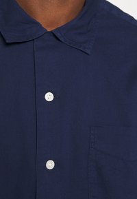 Mörkblå knäppskjorta med klassisk krage, vita knappar och en bröstficka med en subtil textur.