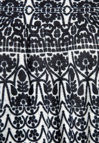 Tessuto a fantasia bianco e nero caratterizzato da design floreali e geometrici con una superficie texture, mostrato in sezioni plissettate.
