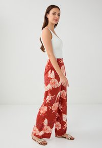 Vloeiende rode bloemenbroek met witte bladerenpatronen, wijde pijpen, lichte stof, elastische tailleband, gecombineerd met een aangesloten witte top.
