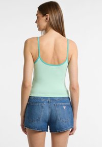 Top a canotta verde menta aderente con spalline sottili, abbinato a pantaloni shorts in denim blu con due tasche posteriori e una patch con il logo.
