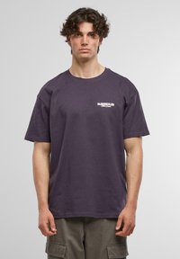 Lilla bomulls t-skjorte med korte ermer, rund hals og en hvit trykket logo på venstre bryst. Enkel design, avslappet passform.