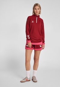 Mørkerød langærmet top med halv lynlås og lyserøde detaljer, parret med mørkerøde shorts med lyserød kant, prydet med hvid chevron-design.