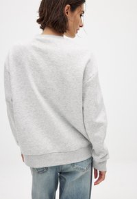 Grijze, oversized sweatshirt met een ronde hals en geribbelde boord. De sweatshirt heeft een zachte textuur en brede mouwmanchetten. Draagt met lichtblauwe jeans.