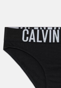 Fekete Calvin Klein alsónemű széles gumírozott derékkal, amelyen jellegzetes fehér "CALVIN" felirat található.