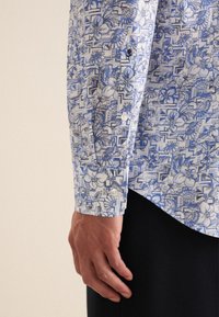 Blauwe en witte gestreepte shirt met bloemmotieven en geometrische ontwerpen; lange mouwen met knoopmanchetten; lichte stof.