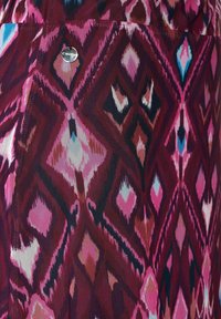 Mönstrad tyg med en blandning av röda, rosa och blå diamantformer, med en metallisk accentknapp. Den texturerade väven tillför djup.