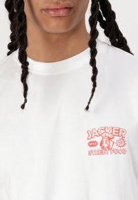 Biela bavlnená tričko s okrúhlym výstrihom, s červenou grafickou potlačou psa kuchára a textom "JACKER STREET FOOD."