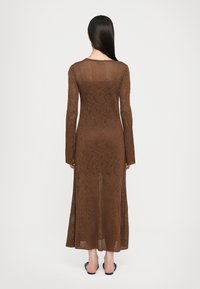 Abito maxi marrone lavorato a maglia con maniche lunghe, caratterizzato da un motivo floreale testurizzato e una silhouette leggermente svasata. Dettaglio della schiena scoperta.