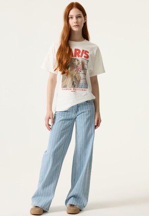 White graphic t-shirt with red "PARIS" text and a floral design, paired with light blue vertically striped wide-leg jeans and beige shoes.